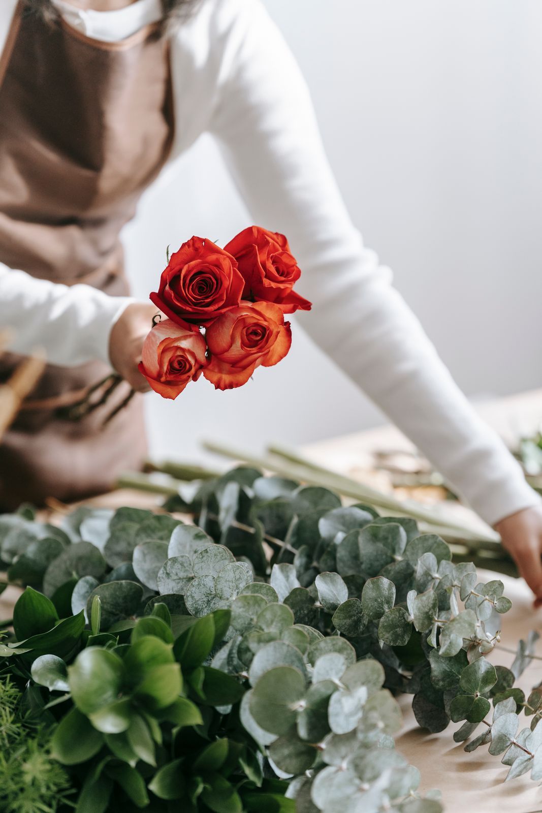 A florist trimming red roses at a table covered in eucalyptus