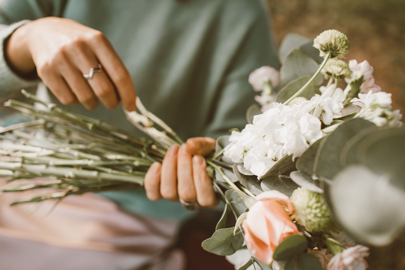 Hands tying white stocks and roses into a bouquet